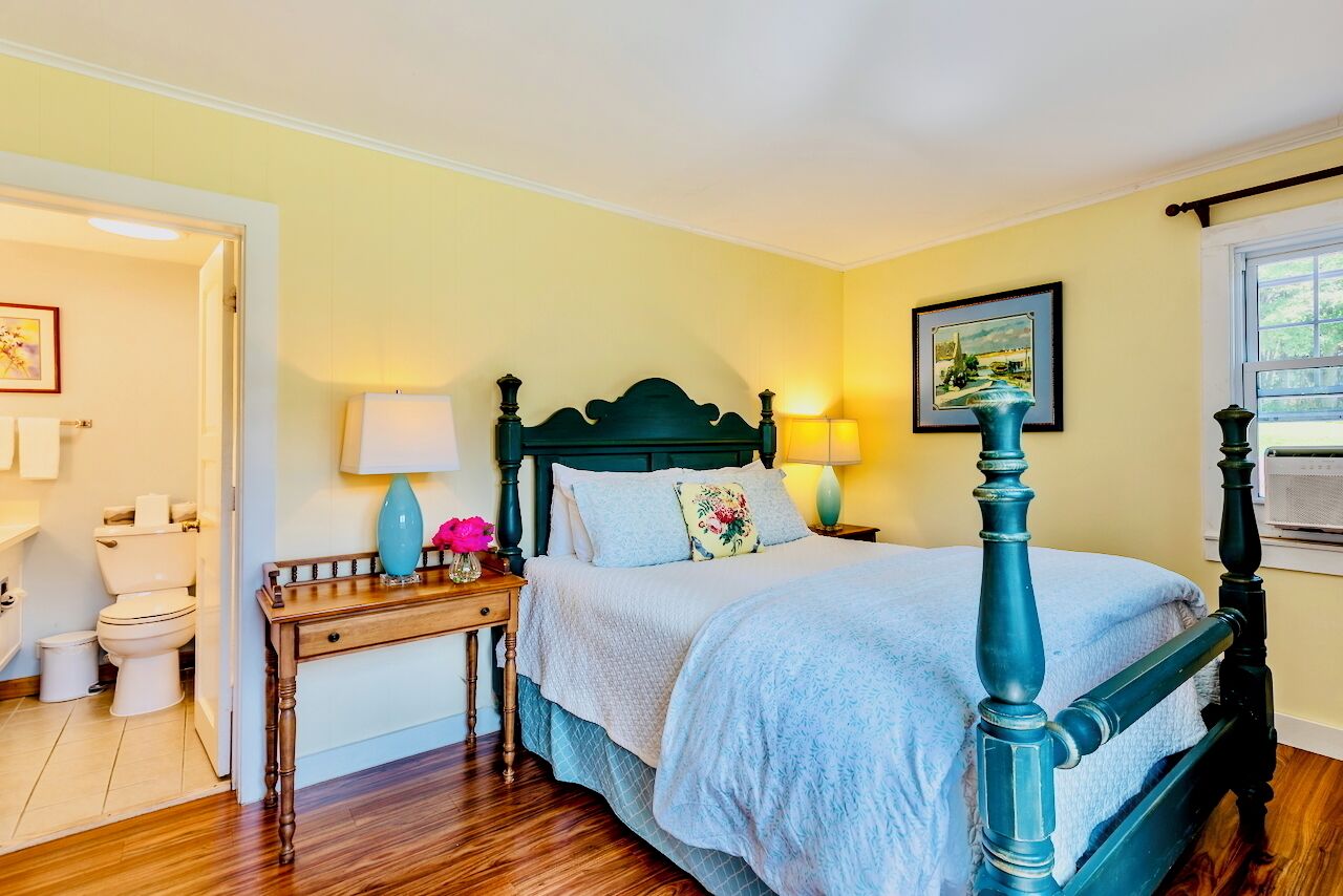 A bedroom with a four-poster bed, a bedside table with a lamp, and a painting on the wall.