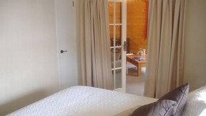 Un dormitorio con una cama, una puerta de madera y vista a un comedor por una puerta de cristal.