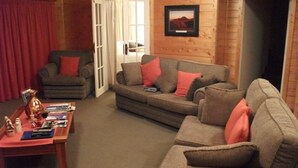 Un salón acogedor con sofá, sillón y mesa de centro, paredes de madera y una puerta que conduce a otra habitación.