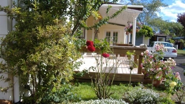Una casa con terraza de madera, rodeada de exuberante follaje y plantas en flor.