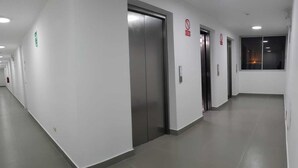 Un long couloir étroit, doté de nombreuses portes, dont celles des ascenseurs, et dont le sol est recouvert de carreaux.