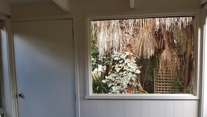 Ein Zimmer mit Fenster und Gartenblick, einer Tür, einem kleinen Korbstuhl und einer Matte auf dem Boden.