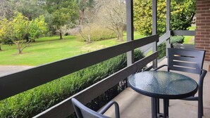 Ein Balkon mit Glastisch und Stühlen, mit Blick auf einen gepflegten Garten mit verschiedenen Bäumen und Sträuchern.