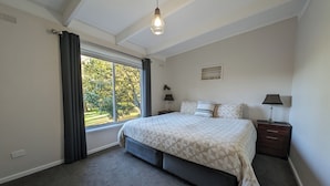 Ein Schlafzimmer mit einem großen Bett, einem Nachttisch mit Lampe, einem Fenster mit Vorhängen und einer Deckenleuchte.