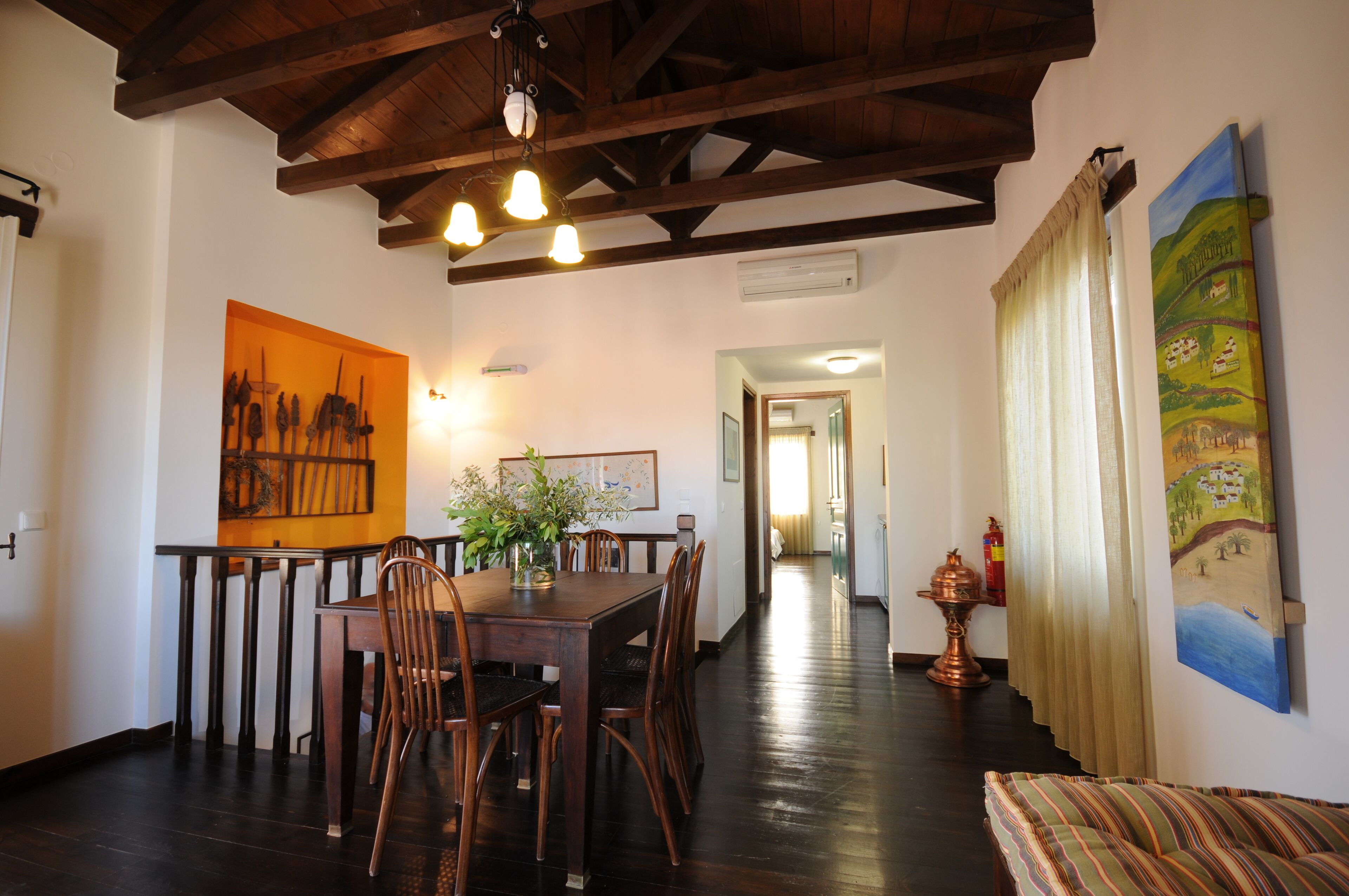 A dining area with a wooden table and chairs, a hanging light fixture, and artwork on the walls.