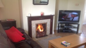 A living room with a fireplace, a leather sofa, a wooden coffee table, and a television. - Cosy cottage near village  beach  Links and Hogs Head Golf Courses (Waterville)