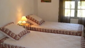A room with two beds, a bedside table with a lamp, a painting on the wall, and a window with curtains.