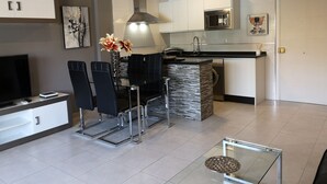 A modern kitchen with a dining area, featuring a black dining set, a glass coffee table, and a TV on a stand. - Beautiful apartment on the beach. A Luxury. (Benalmádena)