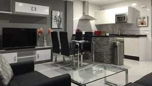 A modern kitchen with a microwave, sink, and a dining area with chairs and a glass table. - Beautiful apartment on the beach. A Luxury. (Benalmádena)