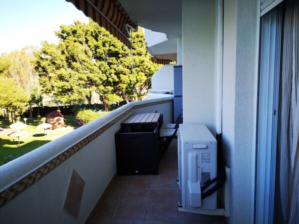 Een balkon met uitzicht op een tuin, een barbecue en een witte airconditioning.