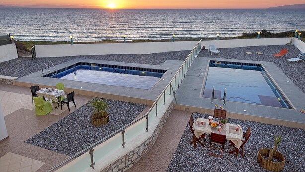 A rooftop pool area with two pools, outdoor seating, and a view of the sunset over the ocean. - Charming Waterfront Villa in South Rhodes , near Monolithos and Prasonissi (Apolakkia)