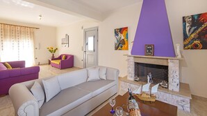 A living room with a fireplace, a sofa, a coffee table, and a door. - Charming Waterfront Villa in South Rhodes , near Monolithos and Prasonissi (Apolakkia)