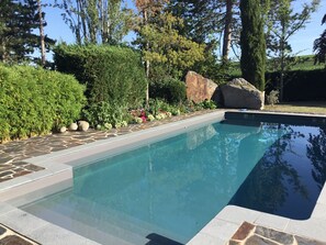 Relax by the pool surrounded by lush greenery and a natural rock feature.