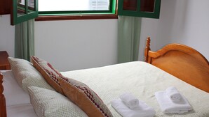 A bedroom with a wooden bed, a window with green shutters, a roll of toilet paper, and a pillow. - Casangeles Holiday Homes (Mozaga)