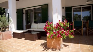 Ein möblierter Terrassenbereich mit einer Couch, einem Couchtisch und einem großen Pflanzgefäß mit rosa Blüten.