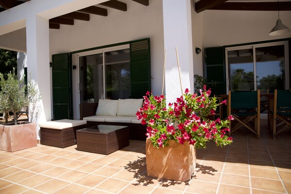 An outdoor patio area with a sofa, a coffee table, and a large planter with pink flowers. - Beautiful 3 Bedroom Villa with Private Pool & Sea Views (Binisafua)