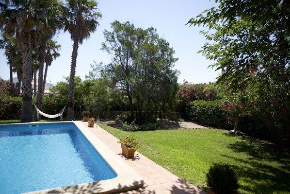 A swimming pool with a tiled deck, surrounded by palm trees, a hammock, and potted plants. - Beautiful 3 Bedroom Villa with Private Pool & Sea Views (Binisafua)