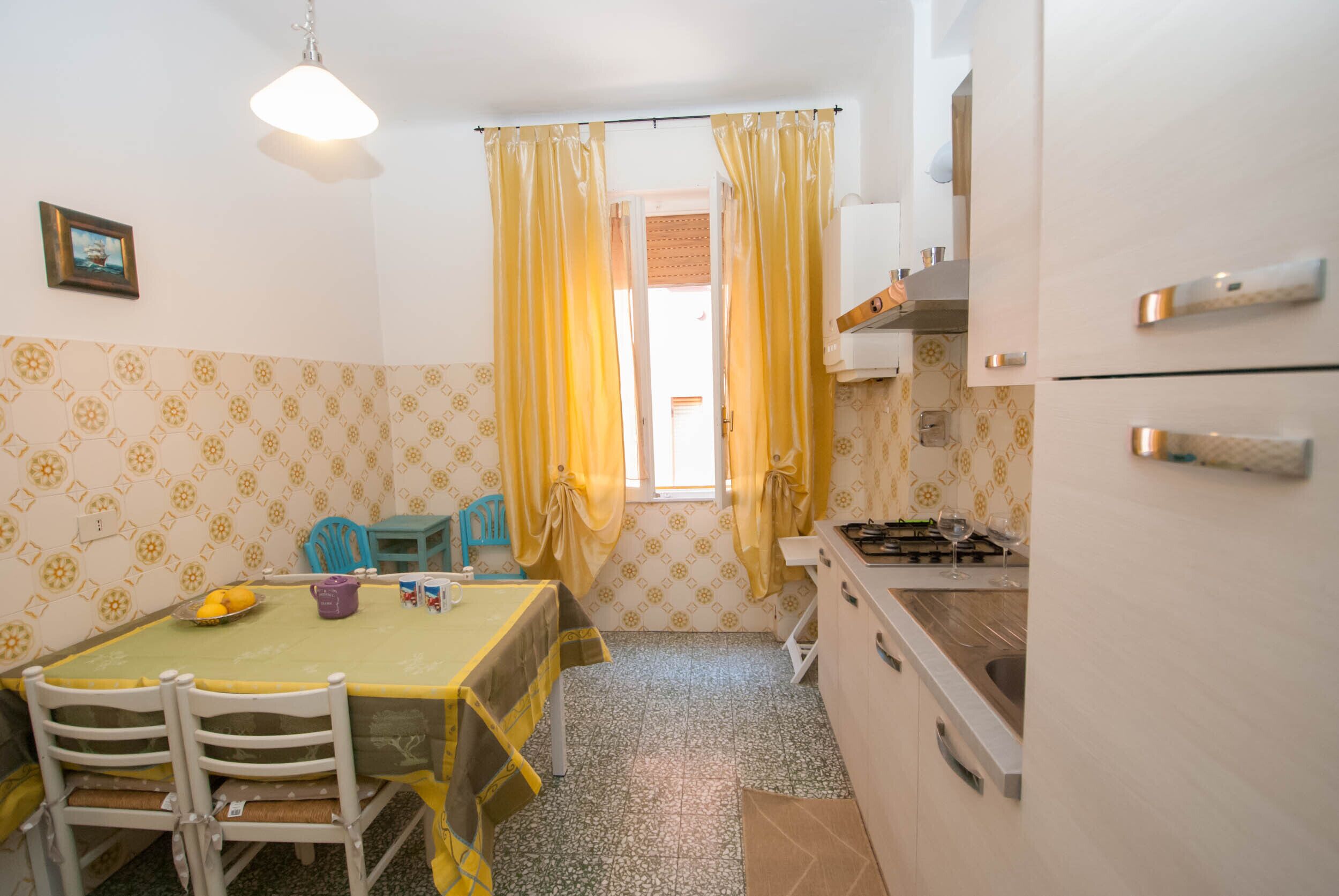 Une cuisine compacte avec un coin repas, comprenant une table avec des chaises, une petite fenêtre avec des rideaux et un réfrigérateur.