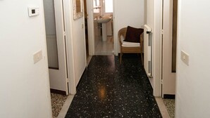 Un couloir avec un sol noir à motifs, des murs blancs et une chaise avec un coussin.