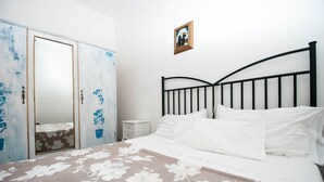 Une chambre à coucher avec un lit, du linge de lit blanc, une table de chevet, une armoire et un tableau encadré au mur.