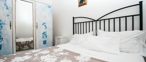 A bedroom with a bed, white bedding, a nightstand, a wardrobe, and a framed picture on the wall.