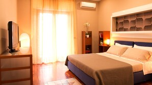 A hotel room with a bed, a television on a stand, a desk, a bookshelf, and an air conditioning unit. - Casa Chicco - My Rental Homes (Sorrento)