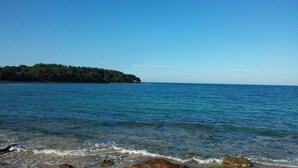 A coastal scene with clear blue water, a rocky shoreline, and a forested island in the distance. - Pet-friendly vacation home right by the sea - last minute promotion 15% discount (Novigrad)