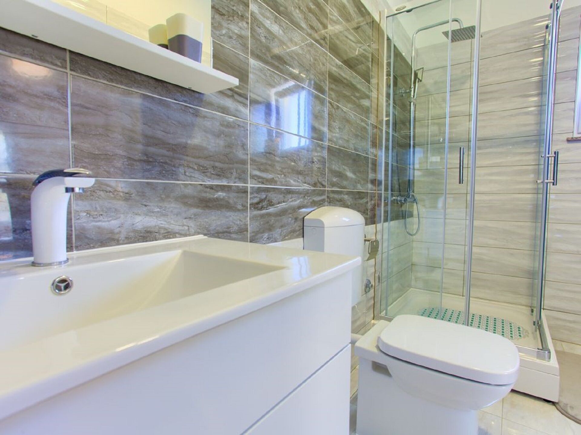 Une salle de bain moderne avec un lavabo blanc, des toilettes et une douche à parois de verre.
