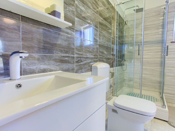 Un baño moderno con lavamanos, inodoro y cabina de ducha de vidrio.