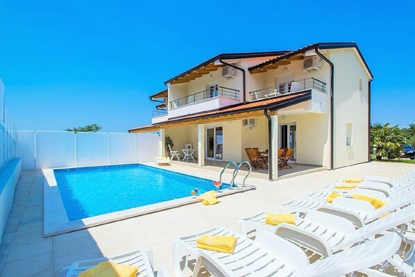 A two-story house with a swimming pool and sun loungers.