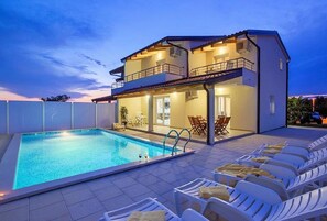 Una casa de dos pisos con piscina y mobiliario de exterior.