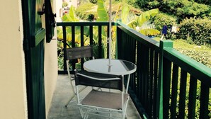 Een balkon met een tafel en stoel, een grote parasol en uitzicht op groen en gebouwen.