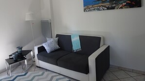 Een woonkamer met een zwart-wit sofa, een kleine tafel met een lamp en een schilderij van een kustlandschap.