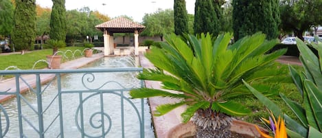 A garden with a fountain, tall trees, and a gazebo.