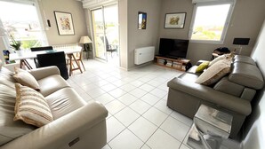Ett rymligt vardagsrum med en soffa, en TV och en matplats med bord och stolar.