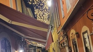 En smal gata med uteservering, ljusslingor och ett julgran.