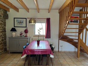 A dining area with a table set for six, a wooden staircase, a stone wall, and a window with curtains. - Lovely, quiet house*** 800 m from Kerlouan beach. (Kerlouan)
