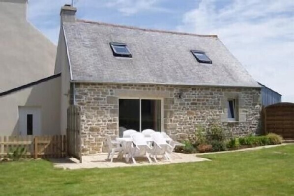 A stone building with a sloped roof and two skylights. There is a patio with white chairs and a table.