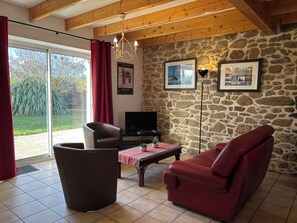 A living room with a stone wall, a television, a sofa, a chair, and a table with a plant. - Lovely, quiet house*** 800 m from Kerlouan beach. (Kerlouan)