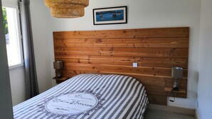 Ett sovrum med en sänggavel i trä, en säng med randigt sänglinne, en hängande lampa i rotting och en inramad tavla på väggen.