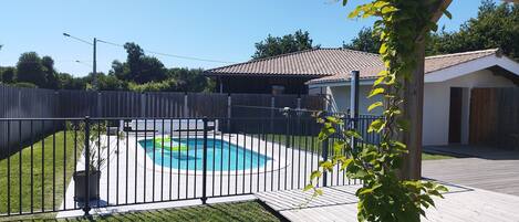 A backyard with a swimming pool, wooden deck, and a fenced area.