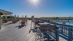 A wooden deck with tables and chairs overlooking a pool and beach. - Stunning Ocean View from top floor Admirals Row 402  (Hilton Head Island)