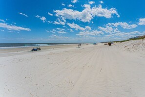 Uma extensa praia de areia com céu claro e algumas nuvens.