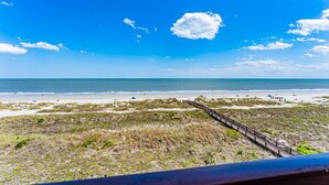 A beach view with a wooden boardwalk leading to the shore, sandy beach, and clear blue sky. - Stunning Ocean View from top floor Admirals Row 402  (Hilton Head Island)