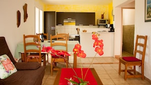 A living room with a sofa, chairs, a dining table, and a kitchen area with a microwave and coffee maker.