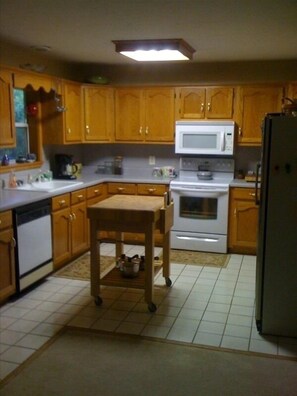 Compact kitchen with a microwave oven, refrigerator, and sink, featuring a small table and dish rack.