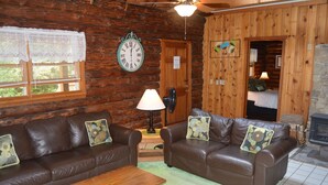 A log cabin interior with two brown leather sofas, a wooden coffee table, a clock, and a fireplace. - Stay WATERFRONT. Stay CHEAT RIVER LODGE (Elkins)