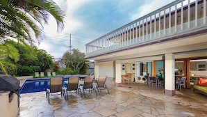 A pool area with stone flooring, outdoor seating, and a covered patio.
