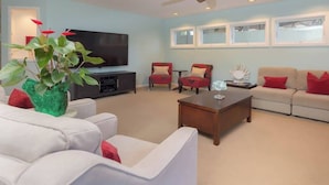 A living room with a flat-screen TV, a coffee table, and seating including a sofa and two armchairs.
