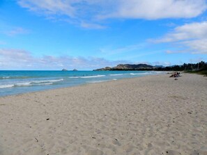 A beach with a clear sky, calm sea, and distant mountains.